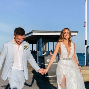 Elegant bride and groom in bespoke wedding attire walking by the seaside.