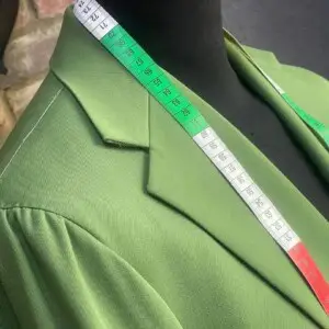 Sharp green bespoke suit fabric with measuring tape draped over shoulder, showcasing tailored craftsmanship. Sharp green bespoke suit fabric with measuring tape draped over shoulder, showcasing tailored craftsmanship.